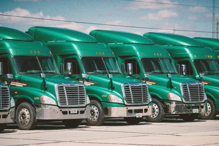 Row of green semi-trucks parked in a fleet under a partly cloudy sky