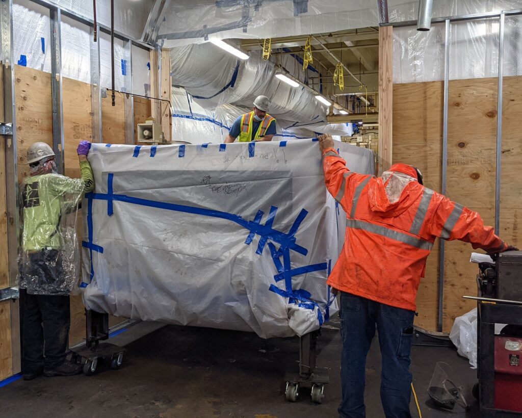 Two workers in a food production facility working to get a decommissioned oven removed